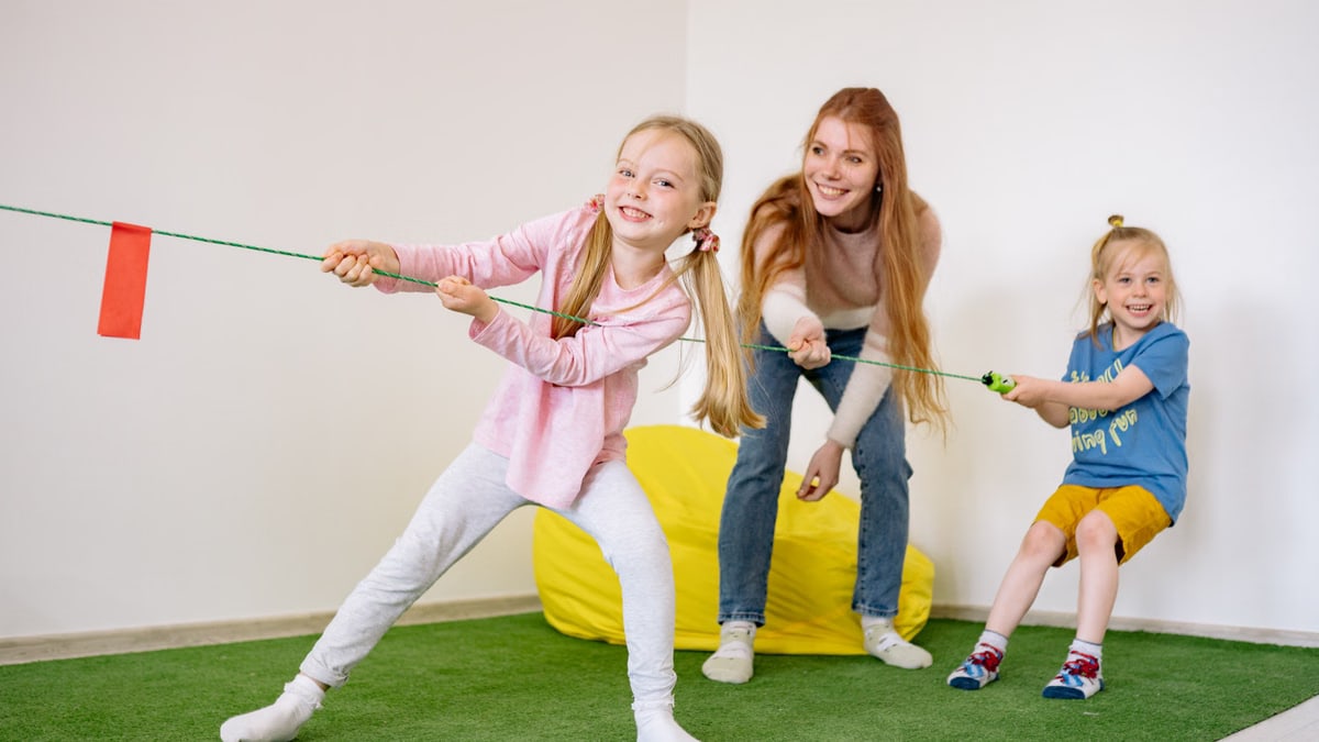 Kids and teacher enjoying a fun tug-of-war game in an indoor playroom setting.